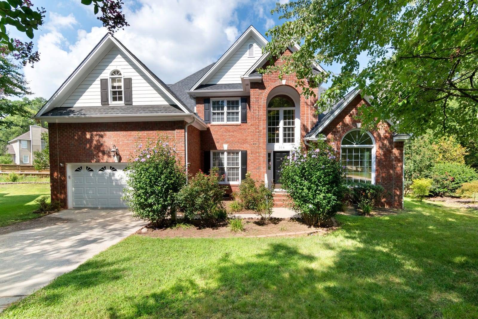 Front of a two-story brick house with a green lawn, shrubs and a driveway