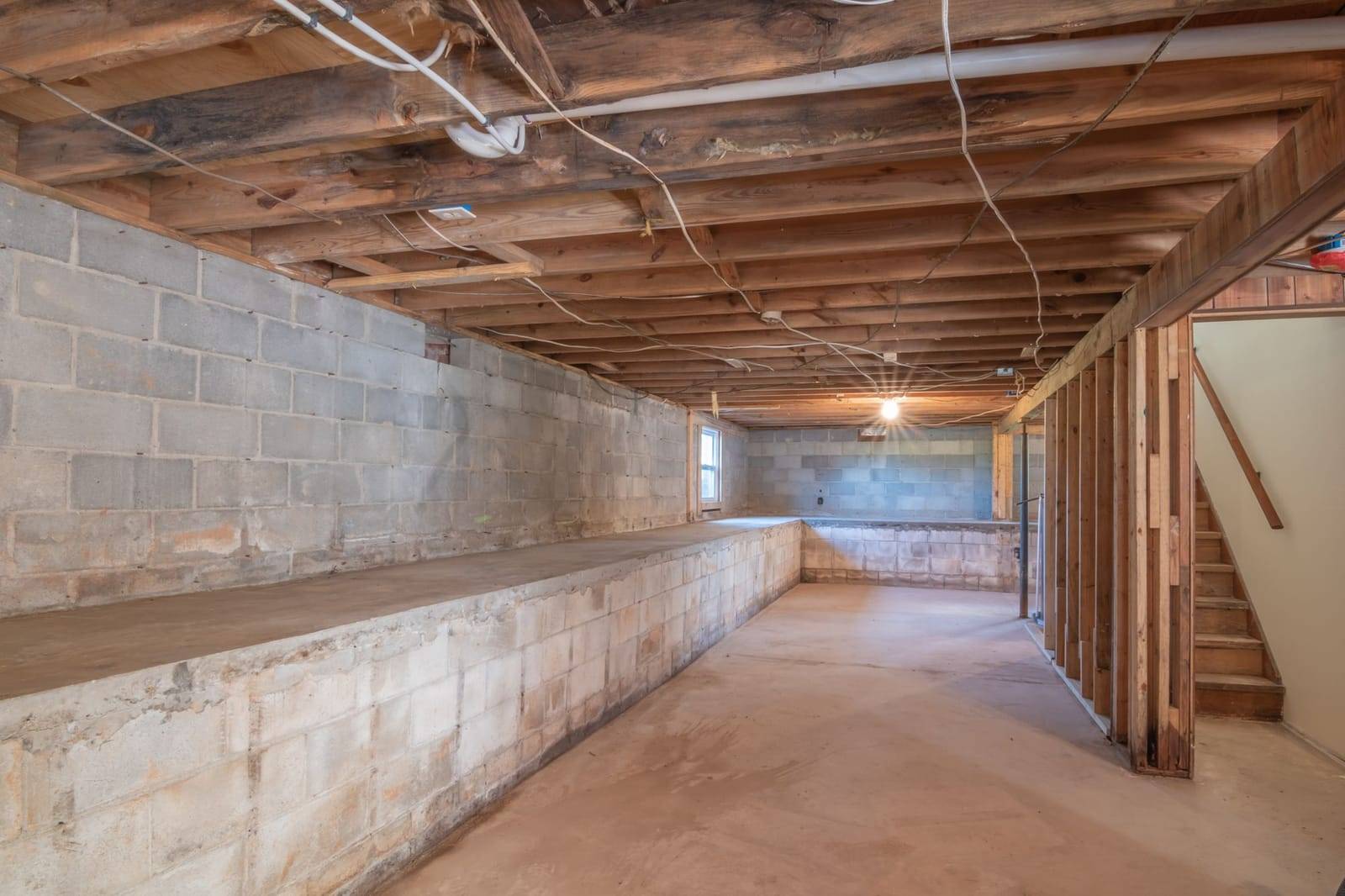 Unfinished lower level with exposed wood floor joists and concrete block walls